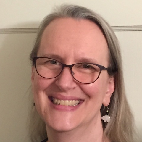 Smiling female tech with glasses, hazel eyes, and shoulder-length blond-brown hair going gray.