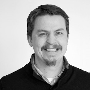 A headshot photograph of Devin Becker, a middle-aged white male with a mustache and goatee.