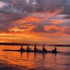 Four rowers in a crew boat at sunrise on the water.